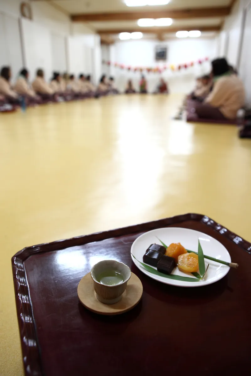 前景为摆有碗的餐盘，参与者围坐在寺院房间内