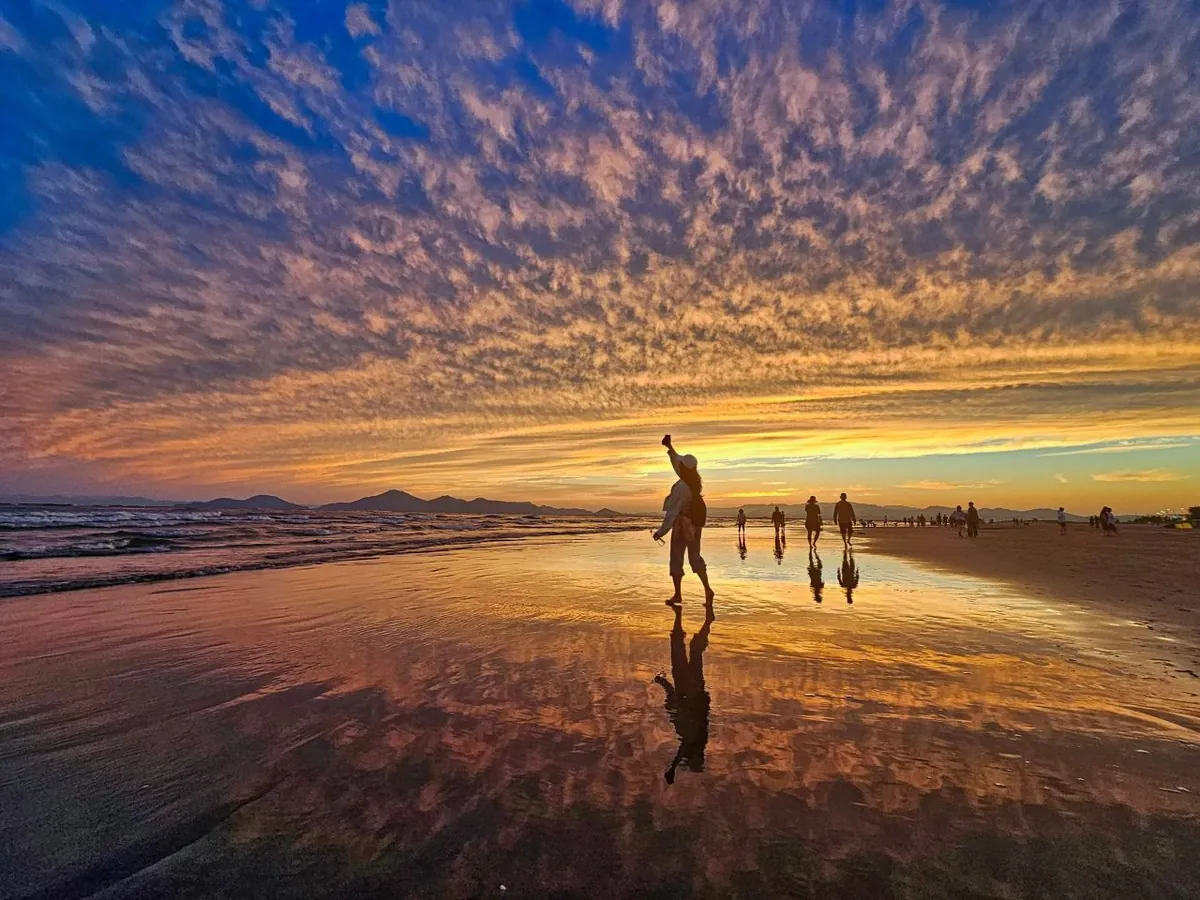 Visitors reflected across wet sand beneath a dramatic sunset at Dadaepo Beach