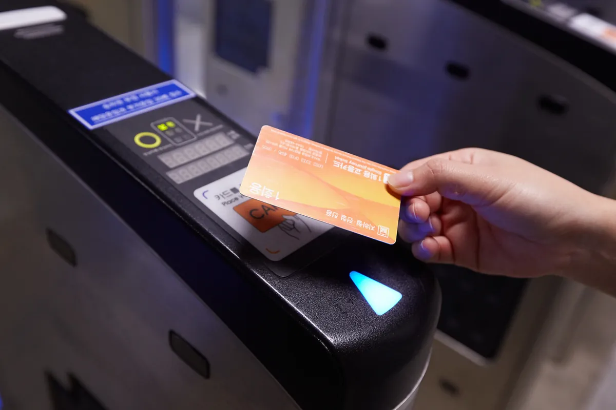 A hand holding an orange ticket card over a subway gate reader