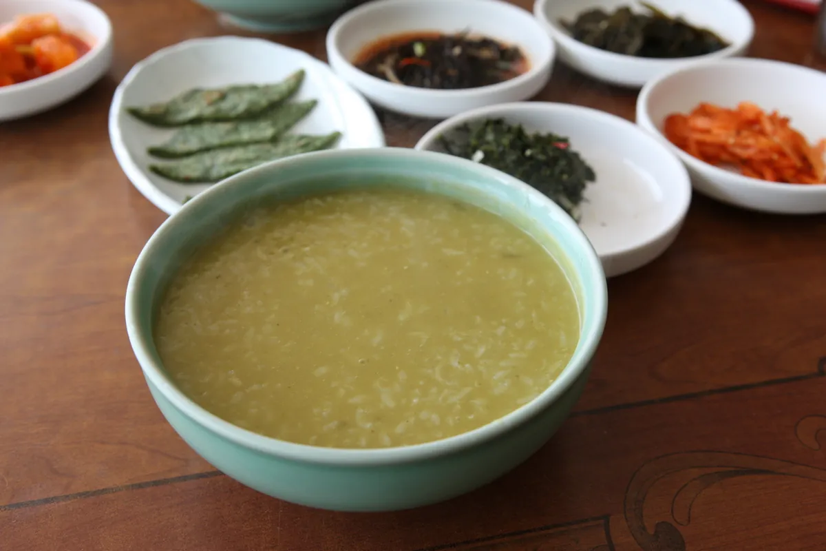 A bowl of abalone porridge with small side dishes on a wooden table