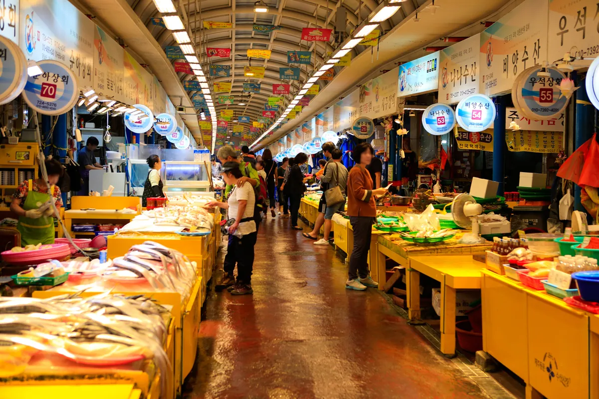Quầy đồ ăn và khách trong lối có mái ở chợ Dongmun Jeju