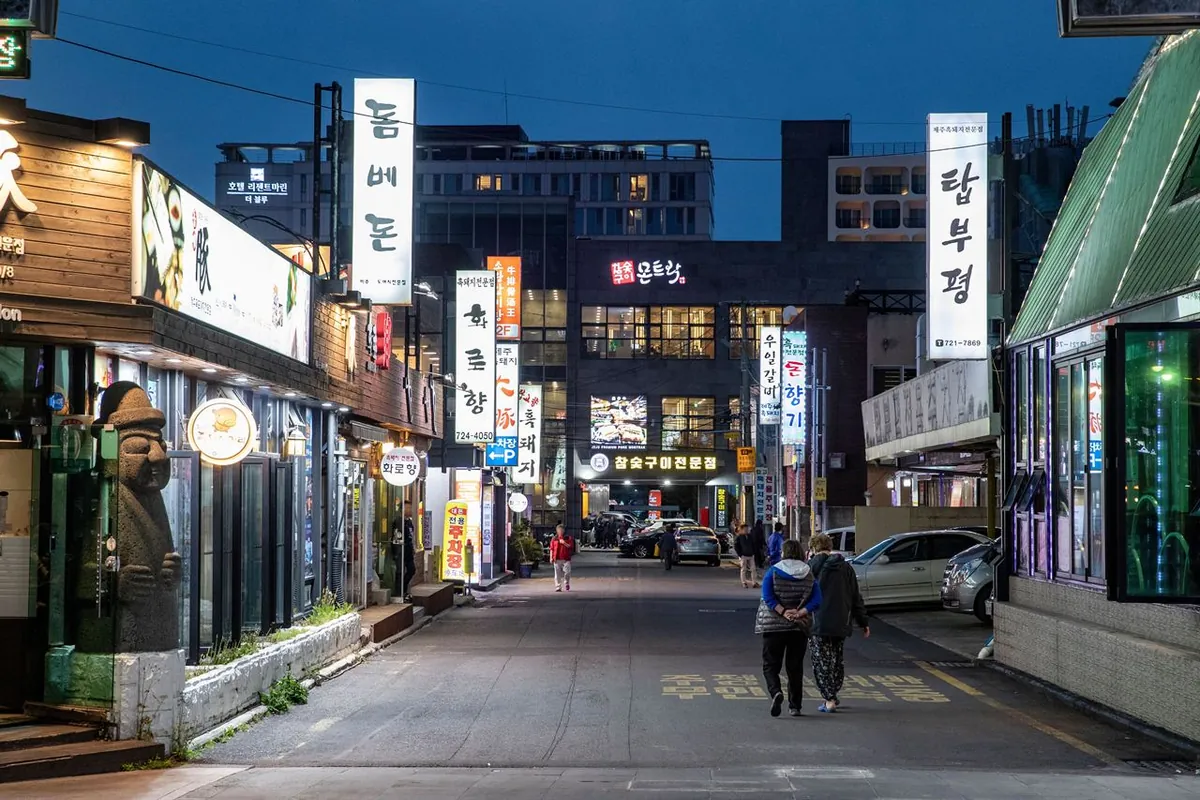 Restaurant signs and entrances along Jeju Black Pork Street at dusk