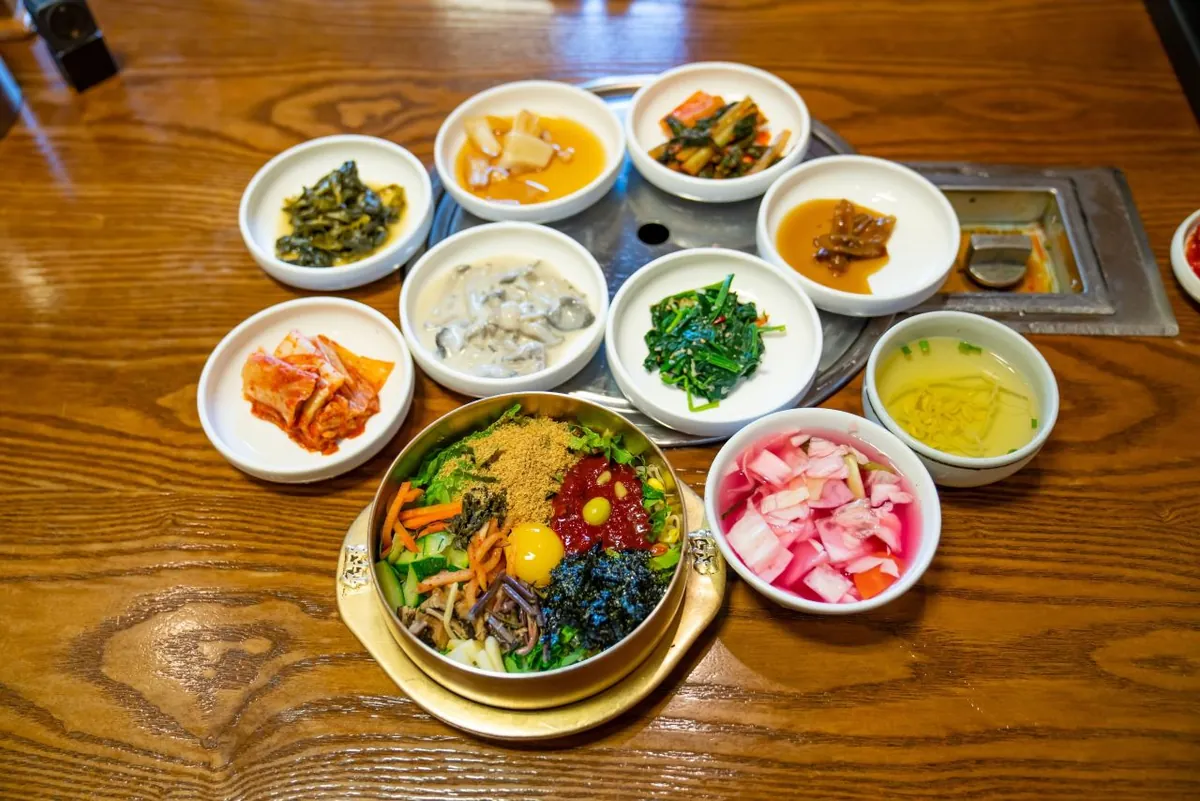 Bát bibimbap đặt trên bàn cùng canh và các đĩa món phụ nhỏ