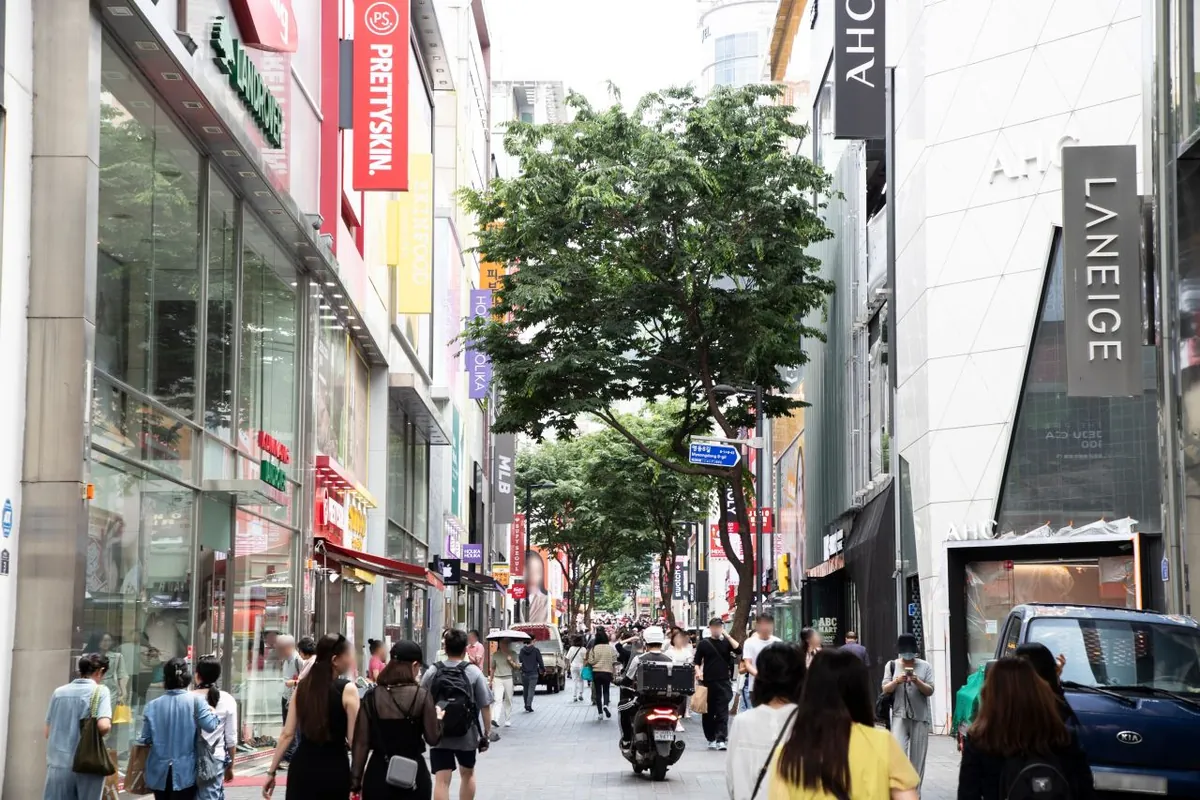 Shoppers walking past tall store signs along a Myeongdong pedestrian street