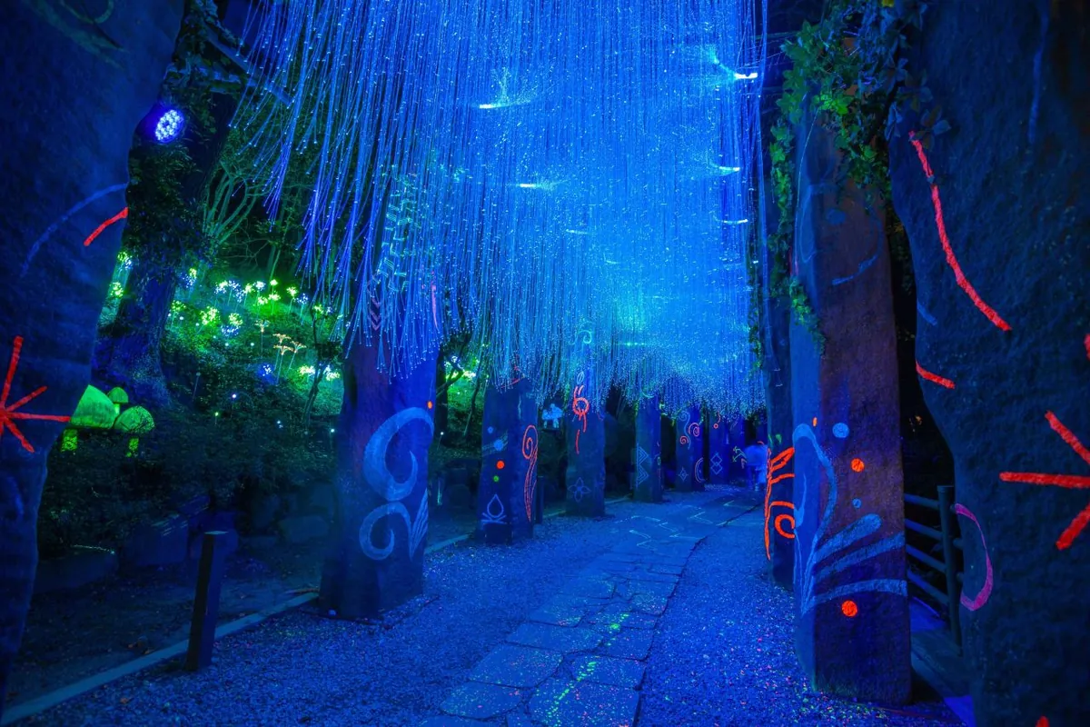 Blue hanging lights and colorful upright forms beside a stone path at DPIRANG
