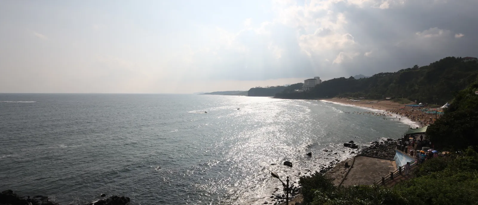 Jungmun Saekdal Beach curves beneath a wooded coastal slope on Jeju Island